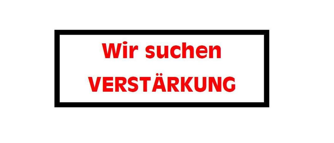 Ein weißes Schild mit schwarzem Rand zeigt roten Text, der 'Wir suchen VERSTARKUNG' lautet. Der Text ist fett und großgeschrieben.