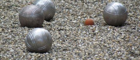 Fünf Metallkugeln liegen auf einer Kiesoberfläche. Vier von ihnen sind grau und eine ist orange.