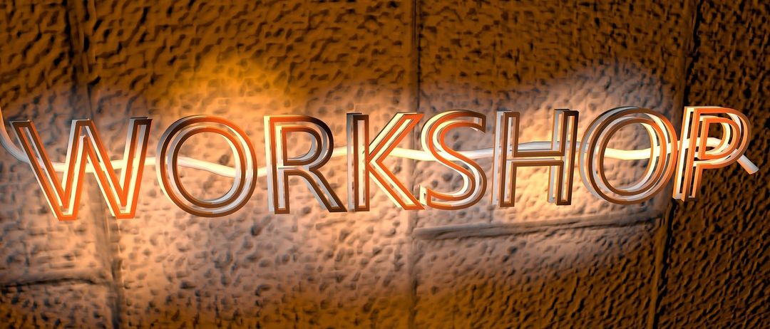 Das Wort Workshop ist an einer strukturierten Wand beleuchtet, mit einem warmen, gelblichen Leuchten, das die Buchstaben erhellt.