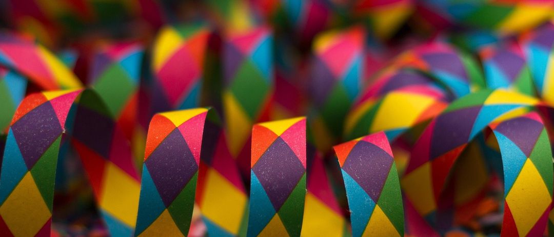 Eine Nahaufnahme von bunten Papiergirlanden, die zu Spiralen gefaltet und möglicherweise für eine Feier auf einer Oberfläche verstreut sind.