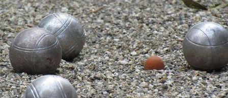 Four metallic balls, three larger and one smaller, rest on a gravel surface. The larger balls are gray, while the smaller one is reddish-brown.