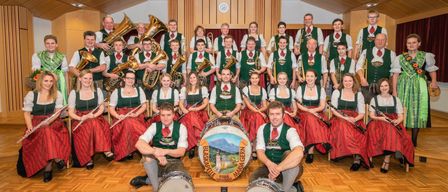 Eine Musikband in grünen und roten Outfits posiert für ein Foto in einem Raum. Das Schlagzeug hat die Worte 'Maria Gern' darauf.
