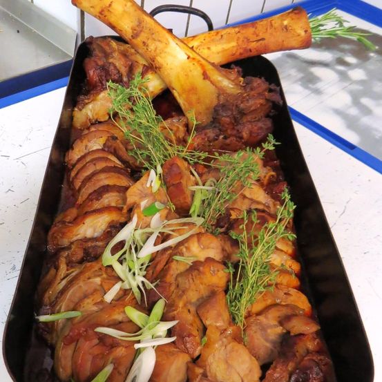 Ein Tablett mit gebratenem Fleisch, geschnitten und mit Kräutern garniert, steht auf einem weißen Tresen. Knochenmark sitzt obenauf.