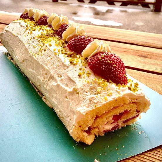 Eine Nahaufnahme eines mit weißer Creme gefüllten Erdbeerkuchens, gekrönt mit geschnittenen Erdbeeren und Pistazien auf einem Holztisch.