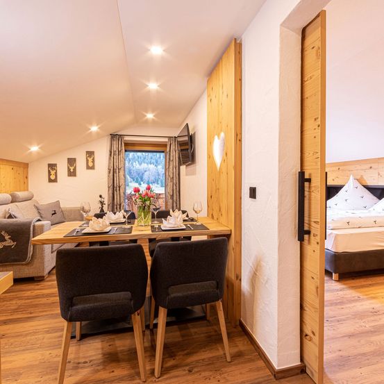 Ein gemütlicher Essbereich mit einem Holztisch und Stühlen, einem Blumenstrauß und einer Couch in der Nähe eines Fensters mit Aussicht.