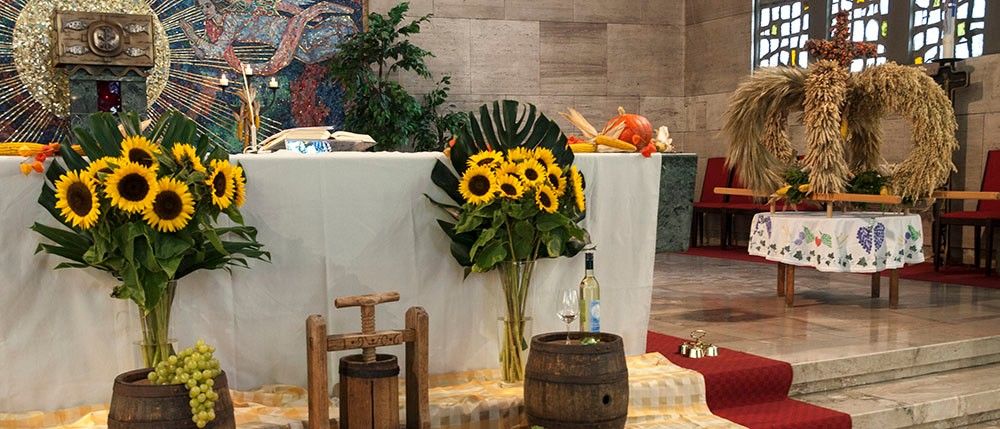 Ein Tisch mit Sonnenblumen und Trauben, eine Weinflasche und ein Weinglas in einer Kirchenumgebung.