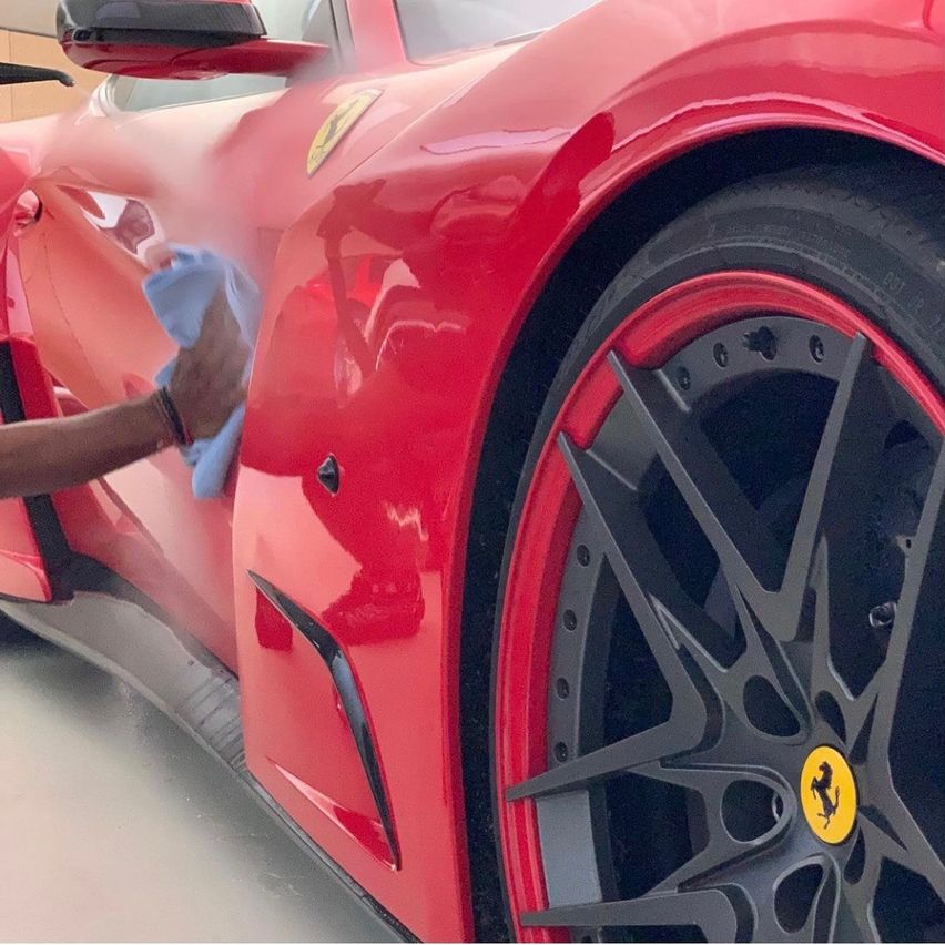 Eine Person reinigt einen roten Ferrari mit einem blauen Tuch. Das Rad des Autos ist detailliert, mit einem gelben Logo.