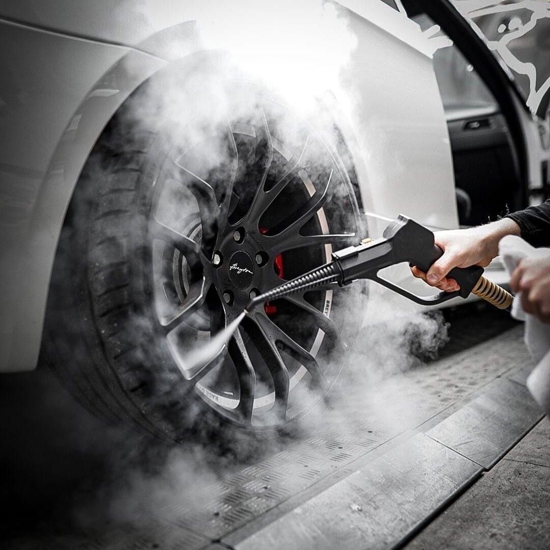 Eine Person reinigt ein Autorad mit einem Hochdruckreiniger. Das Autorad und der Reifen sind mit Schmutz bedeckt.