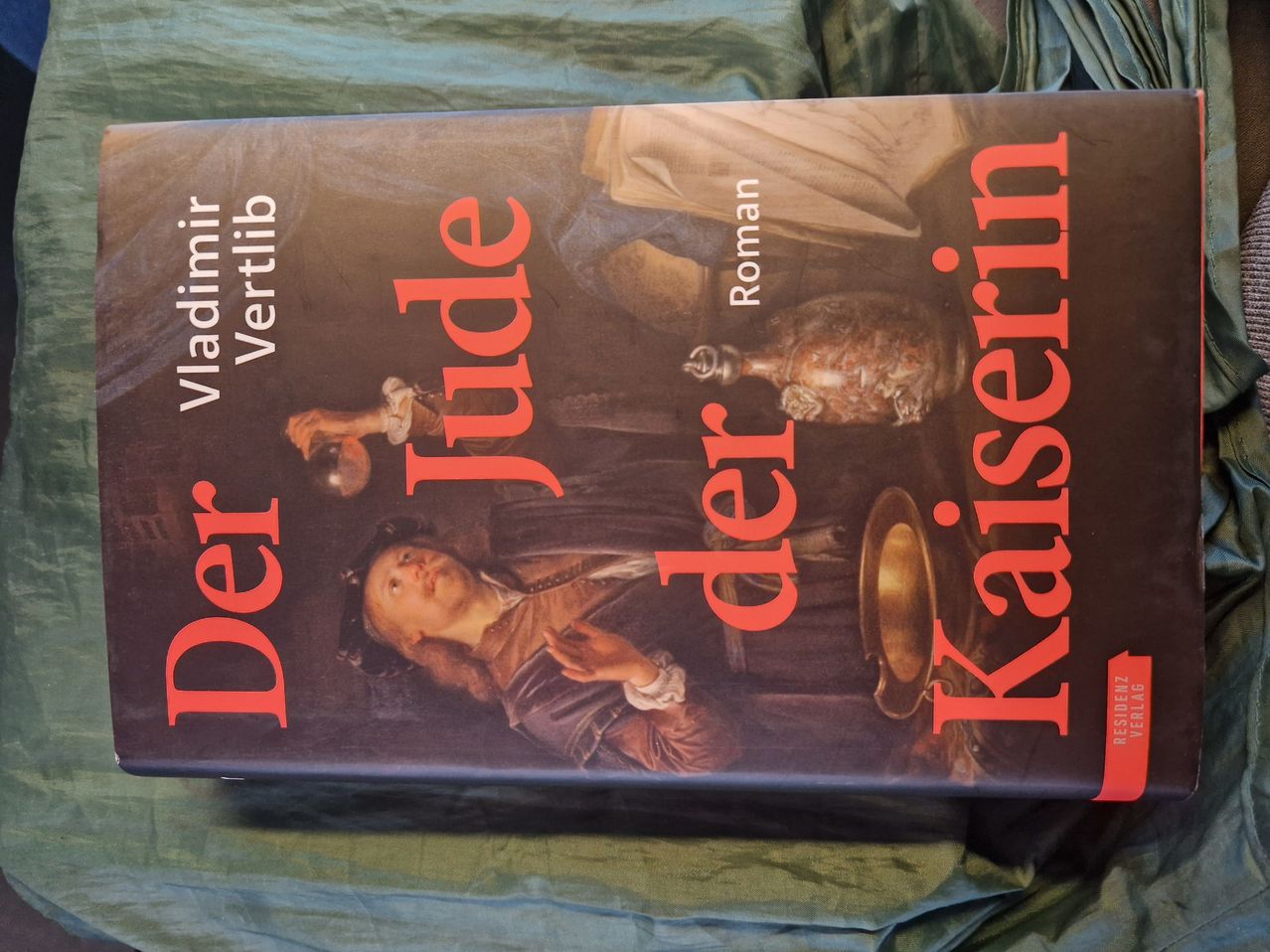 Buchcover von 'Der Jude' von Vladimir Vertlib. Das Cover zeigt eine Illustration einer jungen Person mit einem Becher. Der Titel ist in Rot geschrieben und der Hintergrund ist dunkel.