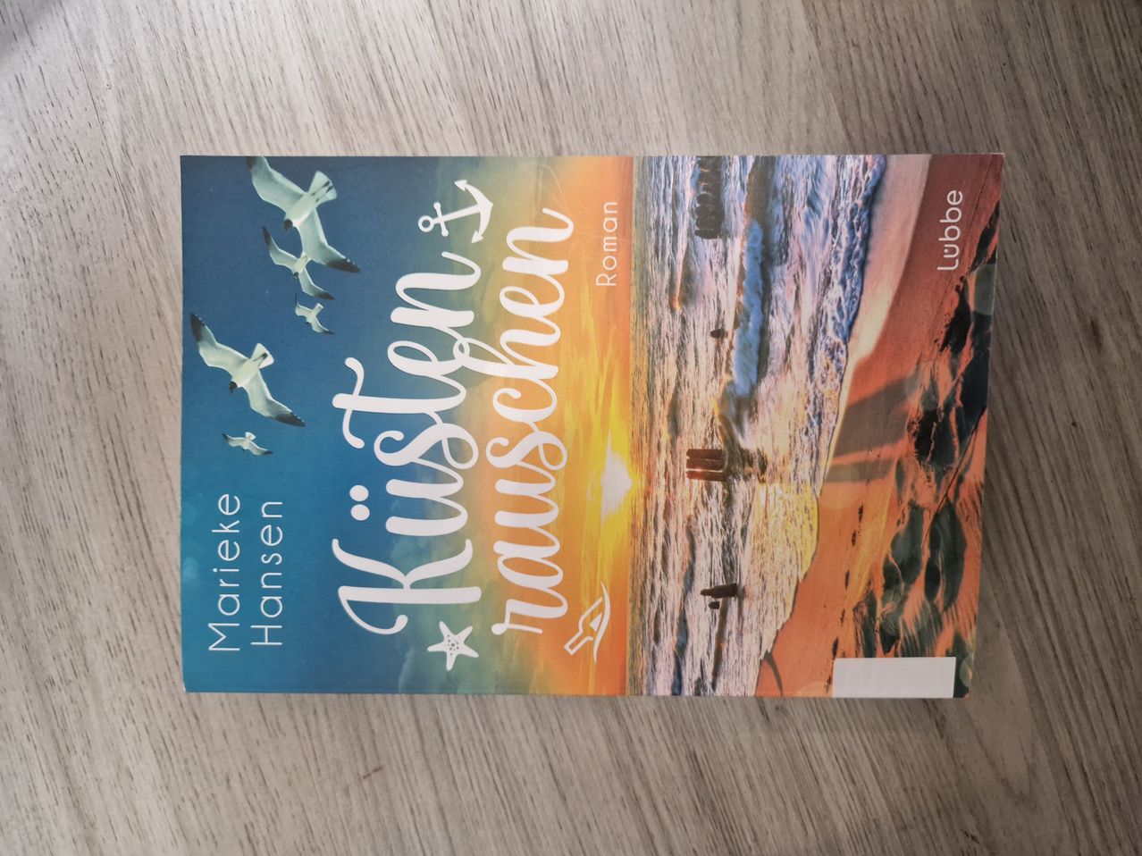 Ein Buchcover mit einem Sonnenuntergang und Möwen, die über dem Ozean fliegen. Der Titel lautet 'Küstenleuchten' und der Autor ist Marieke Hansen.