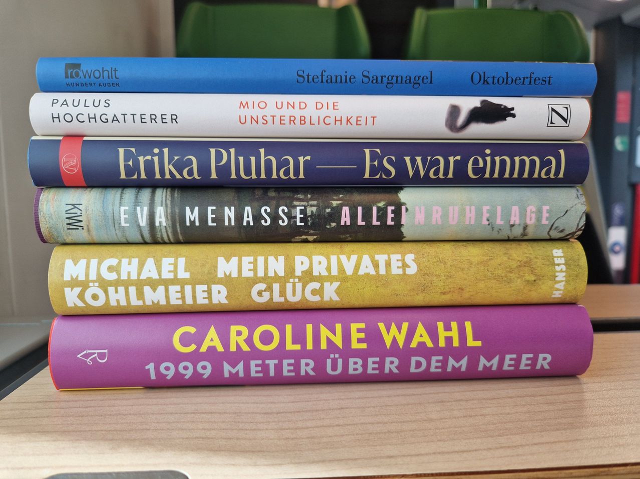 Ein Stapel von fünf Büchern auf einem Holztisch. Von oben nach unten: 'Wohlt', 'Stefanie Sargnagel', 'Erika Pluhar', 'Michael Kohlmeier', 'Caroline Wahl'.