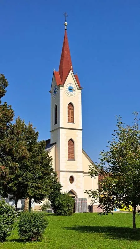 Eine Kirche mit einem roten Turm und einer Uhr ist von grünem Gras und Bäumen umgeben an einem sonnigen Tag.