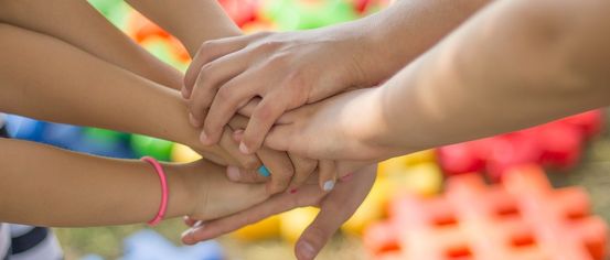 Eine Gruppe von Kindern, die sich an den Händen halten, vor einem farbenfrohen Hintergrund. Sie sind in einem Kreis versammelt, mit ineinander verschlungenen Händen.