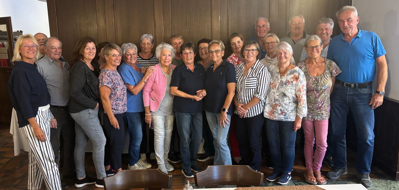 Eine Gruppe älterer Frauen und Männer lächelt und posiert für ein Gruppenfoto in einem Raum.