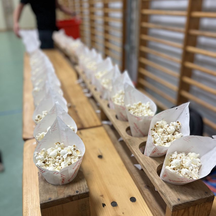 Eine Reihe von Holzboxen mit Popcorn in Papiertüten, auf einem Holztisch angeordnet, mit einer Person dahinter stehend.