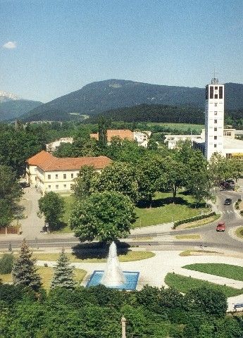 Eine Vogelperspektive einer Stadt mit einem großen Gebäude, einem Brunnen, Bäumen und Bergen im Hintergrund.