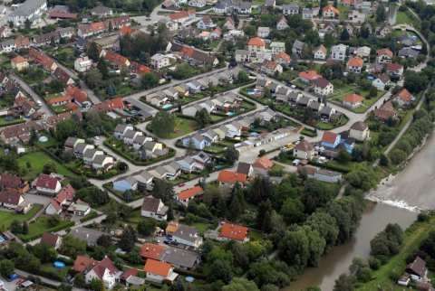 Luftaufnahme eines Wohngebiets mit mehreren Häusern, einige mit roten Dächern, umgeben von Bäumen und einem Fluss.