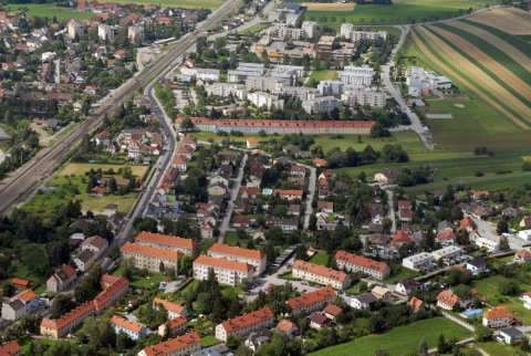 Luftaufnahme einer Stadt mit vielen Gebäuden, einer Eisenbahn und umgeben von grünen Feldern.