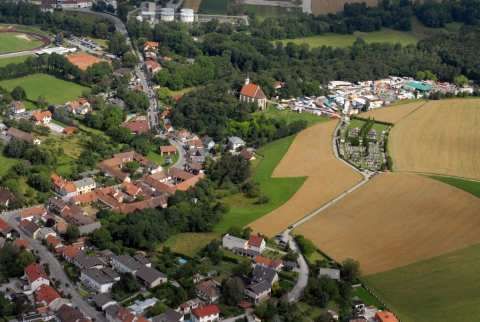 Eine Luftaufnahme einer Stadt mit vielen Häusern und Gebäuden, umgeben von grünen Feldern und Bäumen.