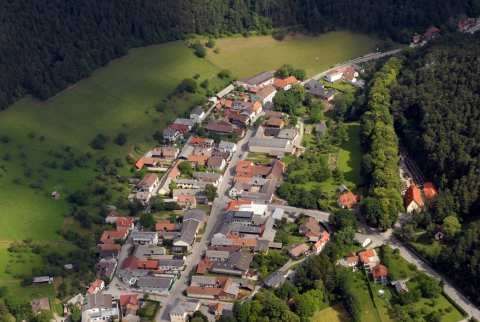 Eine Luftaufnahme eines Dorfes mit vielen Gebäuden und Häusern, umgeben von grünen Feldern und Bäumen.