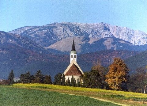 Eine malerische Kirche steht in einem farbenfrohen Feld vor der Kulisse majestätischer Berge.