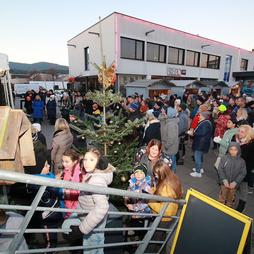 Eine Menschenmenge versammelt sich um einen Weihnachtsbaum vor einem Gebäude mit Schildern und Dekorationen.