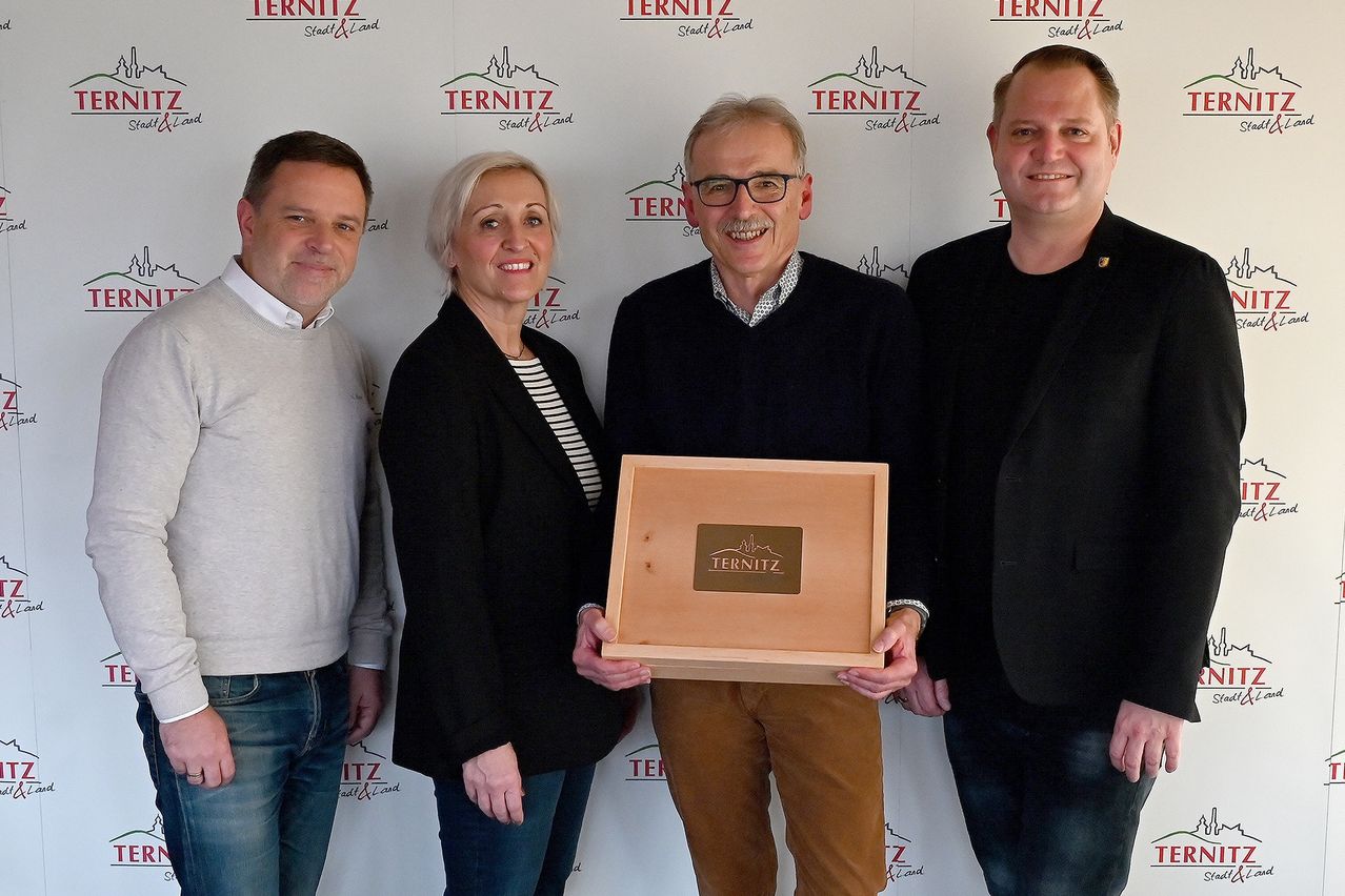 Vier Menschen stehen lächelnd mit einer Holzkiste mit dem Wort Ternitz darauf. Dahinter befindet sich eine Wand mit mehreren Ternitz-Logos.