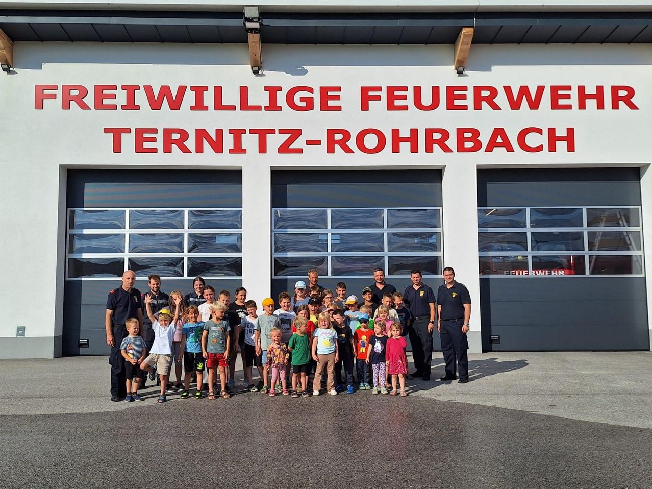 Eine Gruppe von Kindern und Erwachsenen posiert für ein Foto vor dem Gebäude der Freiwilligen Feuerwehr Ternitz-Rohrbach.