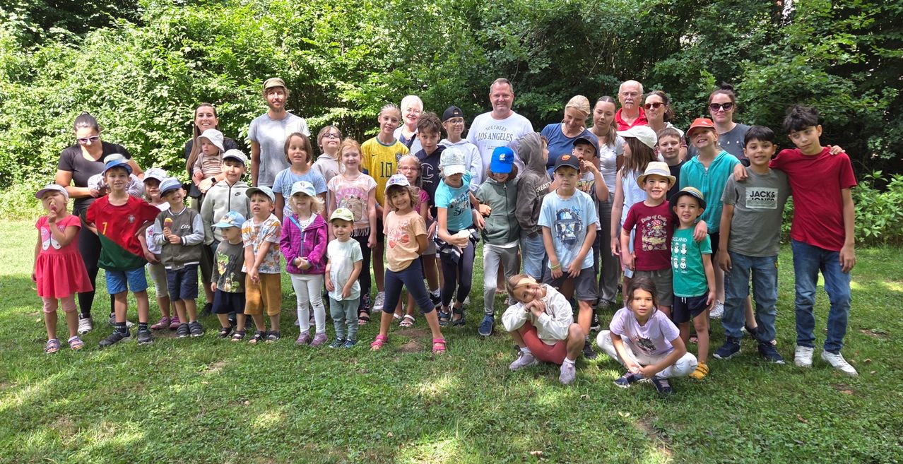 Eine Gruppe von Kindern und Erwachsenen posiert für ein Foto in einem Grasbereich mit Bäumen im Hintergrund.