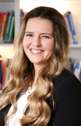 Eine Frau mit langen blonden Haaren lächelt und posiert für ein Foto vor einem Bücherregal.
