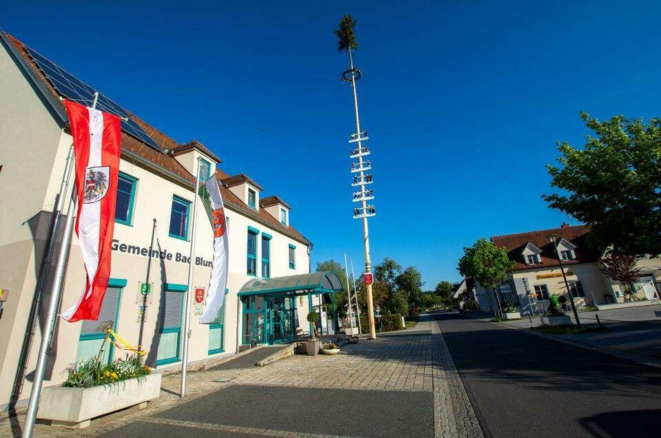  Abschnitt Bild: Das Gebäude der Gemeinde Bad Blun in Deutschland mit Fahnen auf dem Dach und einem hohen Pfahl mit einem Kranz davor.