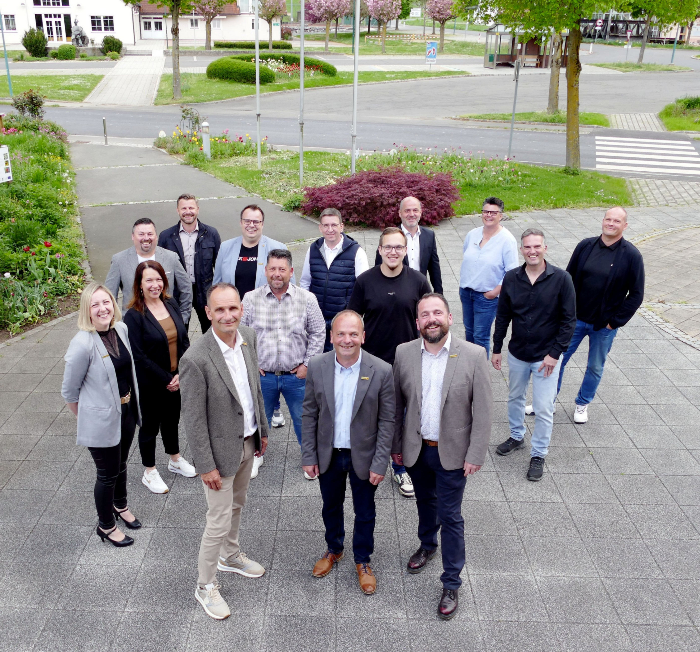 Gruppenfoto der Mitarbeiter von DE-VON vor dem Unternehmen mit Blumen und Bäumen im Hintergrund.