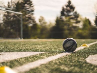 Ein Fußball liegt auf dem Feld mit weißen Linien und einem verschwommenen Torpfosten im Hintergrund.