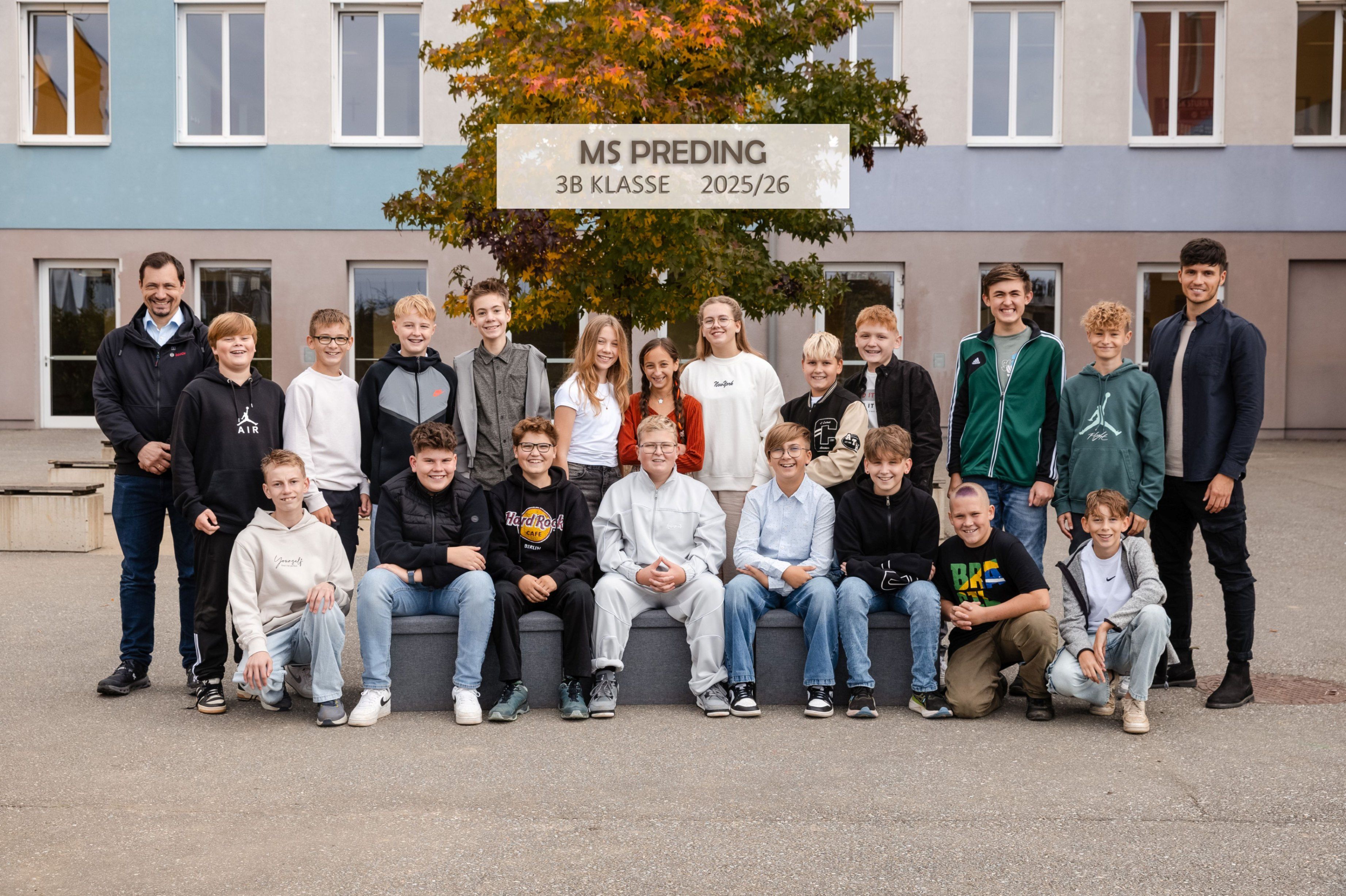 Eine Gruppe von Schülern posiert für ein Foto vor einem Gebäude. Darüber steht ein Schild mit der Aufschrift 'MS Preding 3B Klasse 2025/26'.