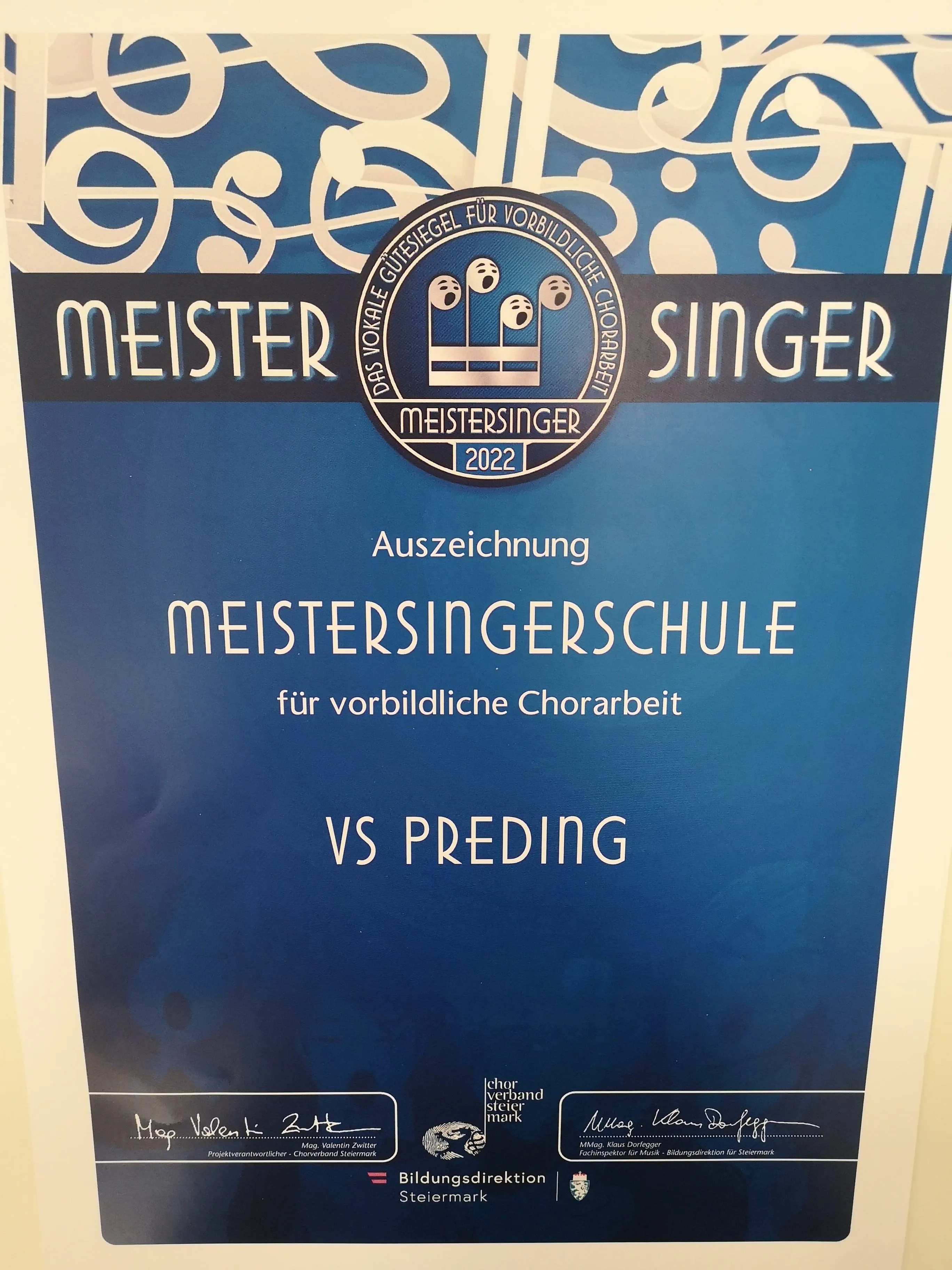 Ein blaues Plakat mit einem runden Emblem, das 'MeisterSinger' liest. Darunter steht 'Auszeichnung' und 'Meistersingerschule'. Der Text 'fur vorbildliche Chorarbeit' ist ebenfalls vorhanden. Das Jahr '2022' ist im Emblem enthalten. Das Plakat ist für einen Chor.