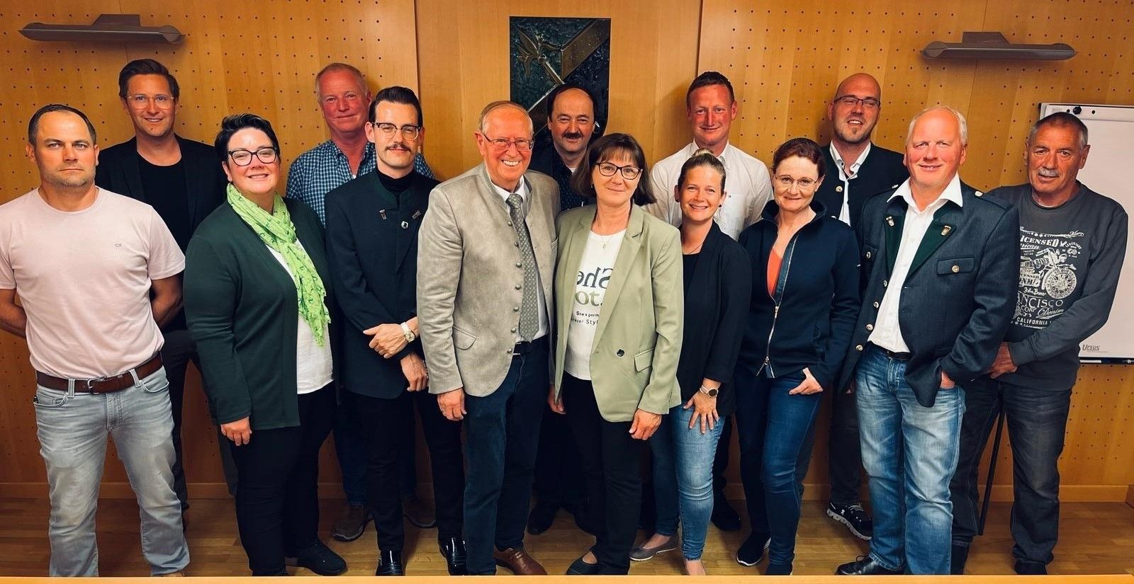 Eine Gruppe von Menschen steht vor einer Wand. Sie alle lächeln und scheinen für ein Foto zu posieren.