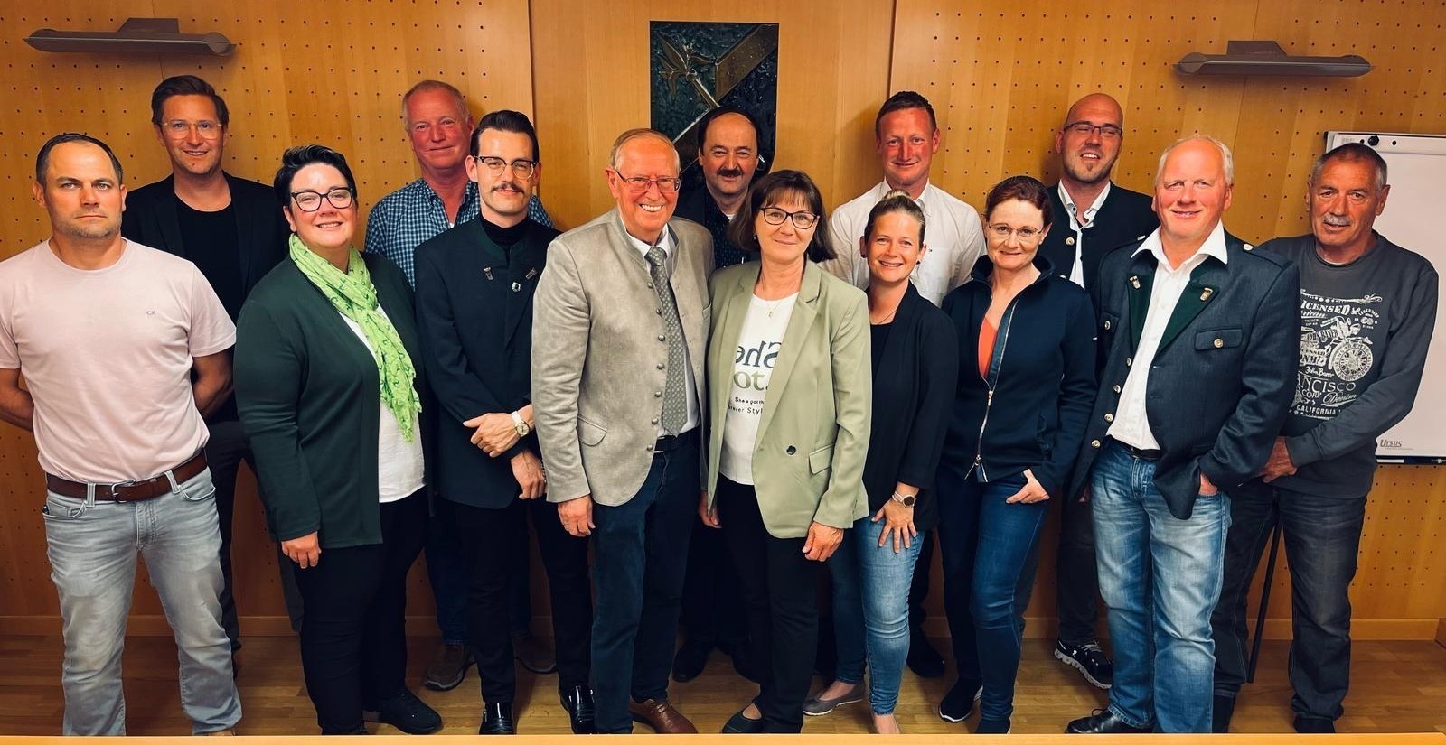 Eine Gruppe von Menschen steht vor einer Wand. Sie alle lächeln und scheinen für ein Foto zu posieren.