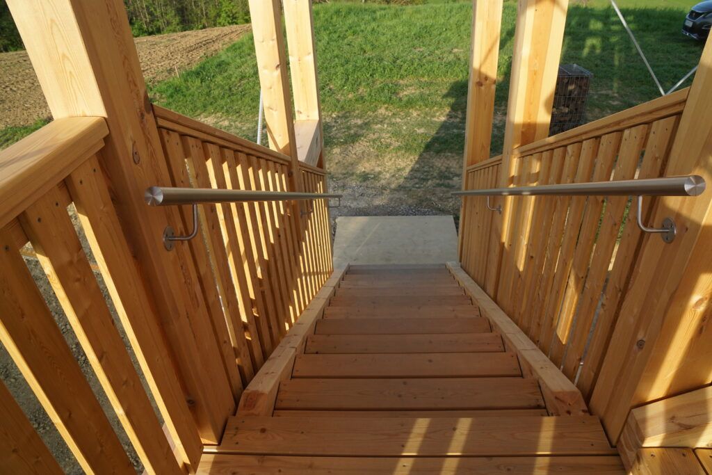 Eine Holztreppe mit einer Metallhandlauf und Holzgeländern, die zu einem Grasfeld mit einem geparkten Auto führt.