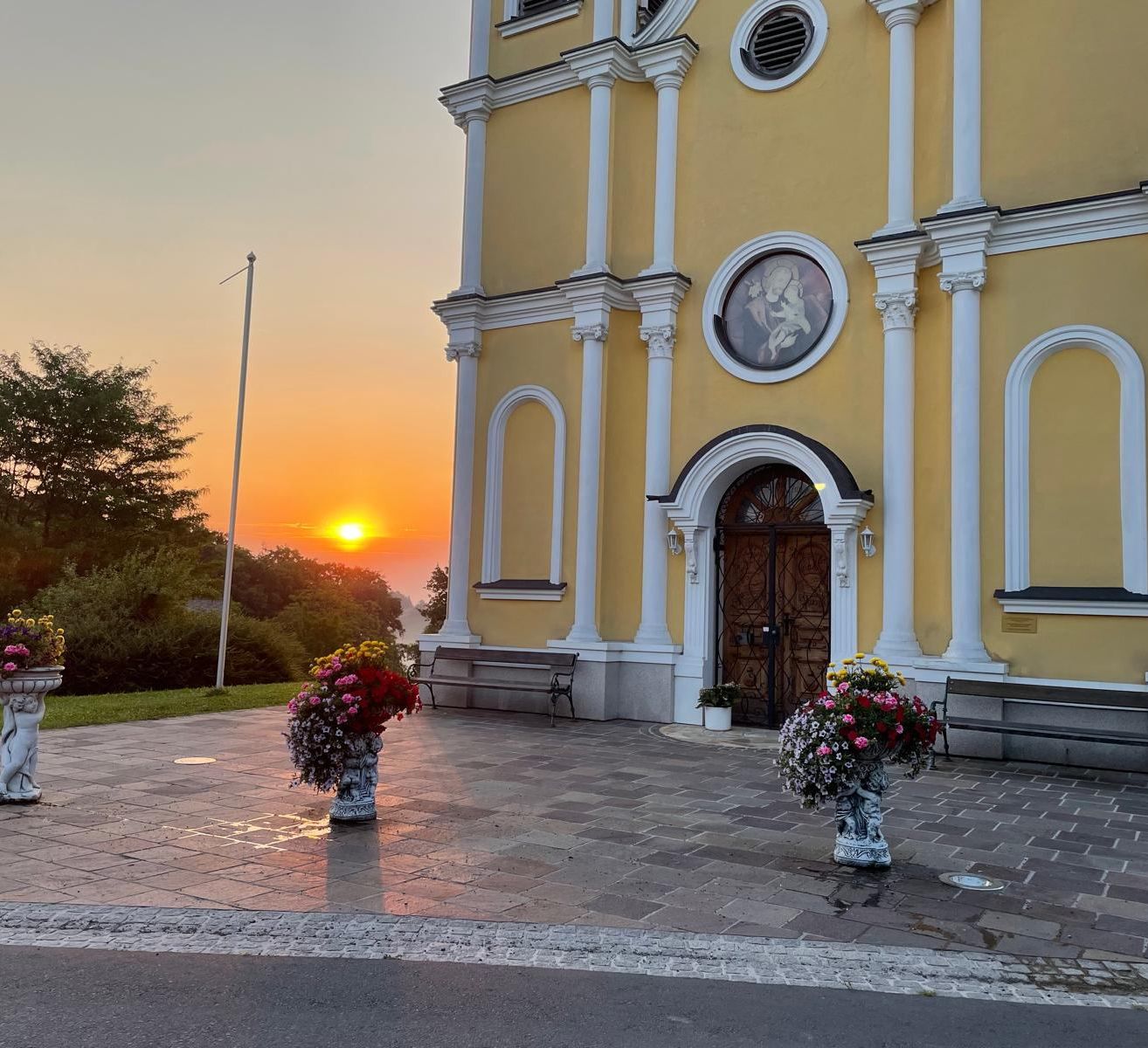 Der Sonnenuntergang hinter einer gelben Kirche mit zwei Vasen mit Blumen davor.