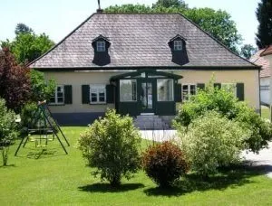 Ein traditionelles europäisches Haus mit einem Schieferdach, umgeben von üppigem Grün und einem Schaukelset im Garten.