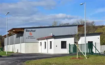 Ein graues Gebäude mit dem Schild Bauhof und einigen Bäumen und Gras davor.