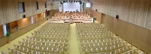 Ein leerer Saal mit Reihen von Stühlen, die zur Bühne ausgerichtet sind, wo wahrscheinlich ein Konzert stattfinden wird.