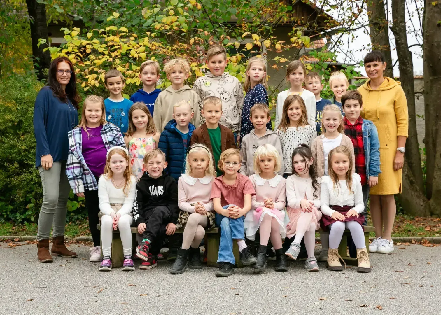 Eine Gruppe von Kindern und zwei Frauen stehen und sitzen draußen. Sie lächeln und posieren für ein Foto.