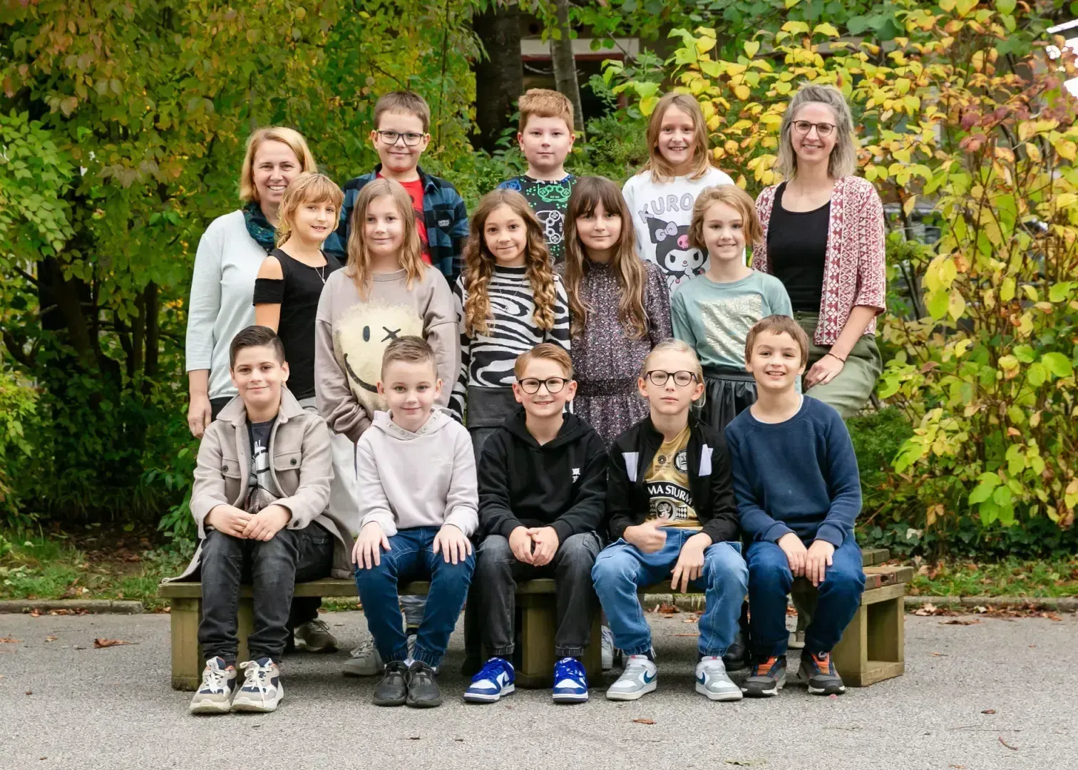 Eine Gruppe von Schülern und Lehrern posiert für ein Foto draußen auf einer Bank mit einem Hintergrund aus Bäumen und Pflanzen.