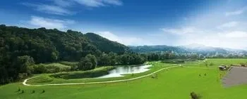 Eine friedliche Landschaft mit einem Golfplatz, einem mäandernden Fluss und üppigen grünen Bäumen unter einem klaren blauen Himmel.