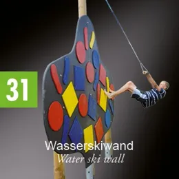 Ein Junge schwingt an einem Seil, das an einer bunten Kletterwand befestigt ist, mit der Nummer 31 auf der linken Seite.