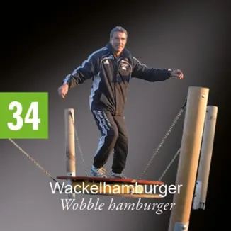 Ein Mann in einer schwarzen und weißen Jacke steht auf einem Holzbrett, das von Ketten in der Luft aufgehängt ist.