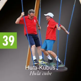 Zwei Männer schwingen auf einer Schaukel, beide tragen rote Hemden, blaue Shorts und Turnschuhe. Ein Mann hält sich an dem Seil der Schaukel fest, während der andere sich an der Sitzfläche der Schaukel festhält.