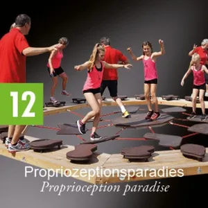 Eine Gruppe von Menschen, einschließlich Erwachsener und Kindern, nehmen an einer Propriozeptionsübung auf einer hölzernen Plattform mit erhöhten Abschnitten teil.