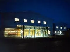 Ein modernes Gebäude mit Glasfenstern und -türen ist nachts beleuchtet. Der Name 'Kulturhaus' ist prominent auf der Vorderseite angebracht.